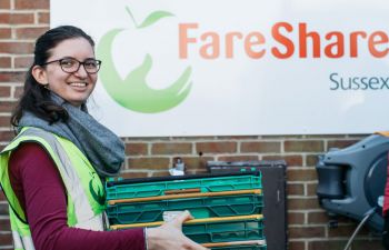 Ƶ student Anna Maukner, wearing a high vis jacket, is carrying plastic containers in front of the FareShare logo