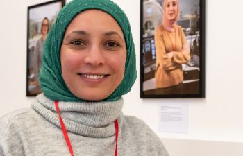 A Ƶ colleague wearing a green headscarf in front of her picture which is part of the exhibition at the Library